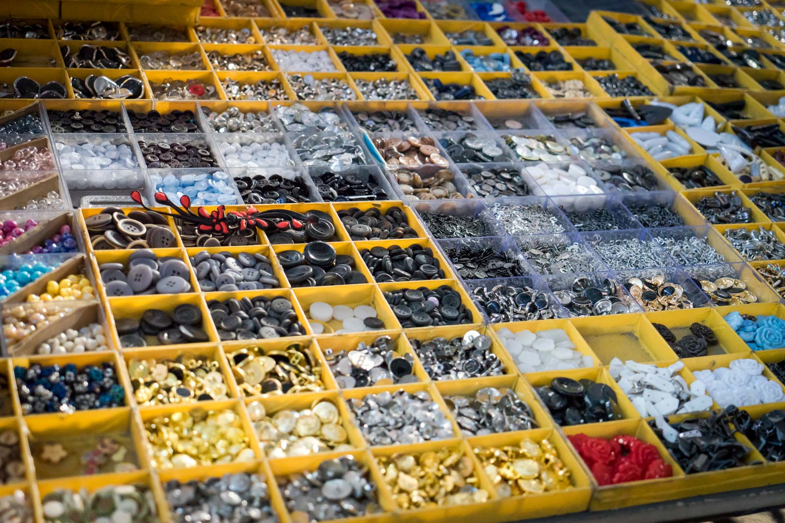 beads and buttons on a tray on a table at a market.
