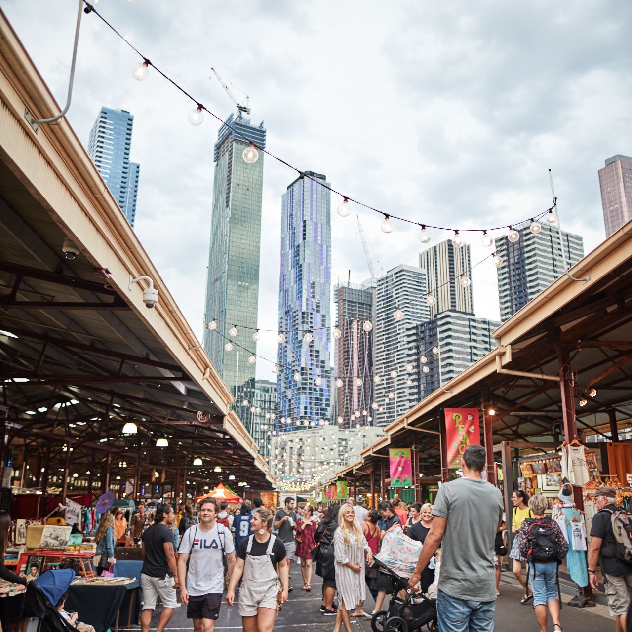 image of outdoor vendor stalls at the Queen Victoria Market in Melbourne with a city view in the background.