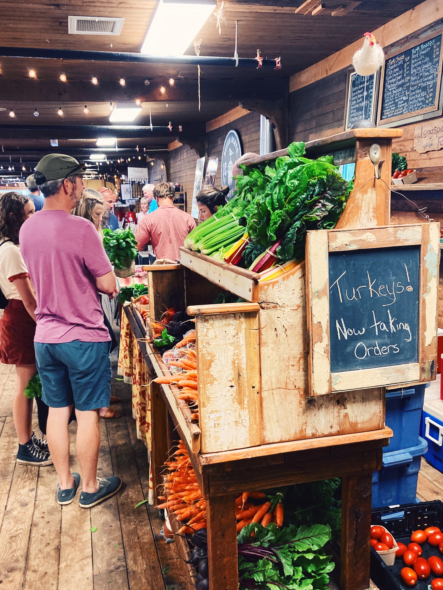 People standing at a fresh produce stand indoors at the Wolfville Farmers Market.