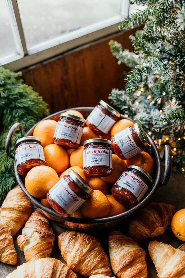 Fresh oranges and preserves in a bowl surrounded by croissants.