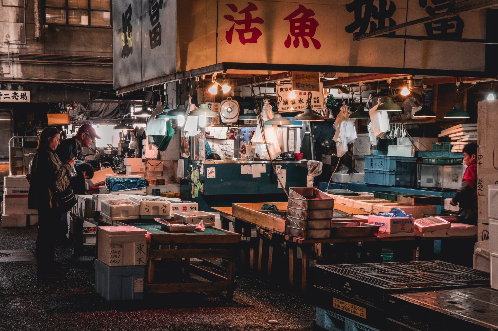 People standing at a fish market stand near the end of the day.